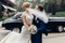 Happy newlywed couple portrait, strong handsome groom lifting up bride in the air, groom carrying beautiful bride outdoors, car in