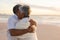 Happy newlywed multiracial senior bride and bridegroom embracing each other at beach during sunset