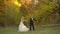 Happy newlyweds is dancing funny against the beautiful autumn landscape with colored fall trees.