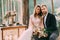 Happy newlyweds look on a photographer. Man and woman in festive clothes sit on the stones near the wedding decoration