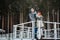 Happy newlyweds stand on a pier on a snowy riverbank in the winter morning