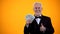 Happy old man in suit holding dollars and showing thumbs-up, business income