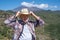 Happy old senior man on mountain hike looking at the camera while holding his hat. Sunglasses and a big smile for the person who