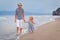 Happy older brother and younger cute sister walking on sea coast