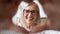 Happy older woman in eyeglasses making heart symbol.
