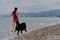 Happy owner of Bernese Mountain Dog on vacation on beach. Caucasian cute red haired woman in swimsuit runs around sea with her