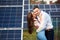 Happy pair are hugging against the background of a row of solar panels at a site near the house.