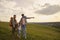 Happy parents and daughter travelers with backpacks hiking in the countryside during the summer afternoon.