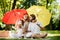Happy parents with two kids have a rest on the lawn under the bright red and yellow umbrellas covering them from the sun
