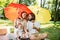 Happy parents with two kids have a rest on the lawn under the bright red and yellow umbrellas covering them from the sun