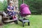 Happy pension age woman takes care of sleeping great grandchild in baby pram, sitting with sphynx cat on wooden veranda at sun