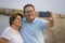 Happy pensioner woman and her husband taking romantic walk taking selfie - happy retired mature couple walking on the beach during