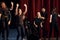 Happy people celebrating success. Group of actors in dark colored clothes on rehearsal in the theater