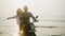 Happy people ride motorbike on seaside at sunrise. Couple in love have fun driving motorcycle on ocean coast. Girl in