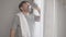 Happy perspiring middle aged man with towel on shoulder drinking water, wiping mouth with hand, and looking at camera