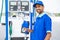 Happy petrol pump worker standing by holding fuel nozzle while looking camera at gas filling station - concept of