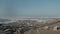 Happy photographer woman walks under very strong wind at cold winter sea shore, thick sea foam flying away slow motion.