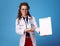 Happy physician woman pointing at clipboard on blue