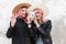 Happy pink-haired girl with smile in straw hat in fashion jacket stands next to girlfriend with modern camera in jacket and shows