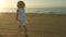 Happy playful little girl in white dress running on the beach sand