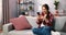 Happy pleasant millennial woman relaxing on comfortable couch, holding smartphone in hands. Smiling young lady chatting