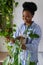 Happy pleased young African woman holding potted Philodendron plant enjoying home gardening