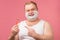 Happy plump man with shaving foam on his face and razor isolated on pink