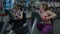 Happy plus-size Caucasian woman cycling exercise bike with slim young lady working out at background. Two positive