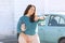 Happy plus size woman posing outside of the blue rental car in sunny day