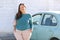 Happy plus size woman posing outside of the blue rental car in sunny day