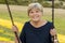 Happy portrait of American senior mature beautiful woman on her 70s sitting on park swing outdoors relaxed smiling and having fun