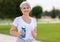 Happy positive mature woman with broad smile holding water bottle while doing sport in city park