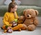 Happy positive pretty girl child in warm yellow knitted comfortable home sweater sitting on floor and playing with teddy bear