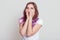 Happy positive stylish female wearing white casual t shirt having lilac hair laughing happily, covering face with palms,