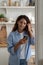 Happy positive woman in casual clothes smiling looking at phone screen standing in kitchen at home