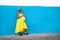 Happy pregnant african woman in yellow dress holding her belly in hands, smiling, posing on the blue wall outdoor. Real people
