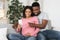 Happy pregnant black couple using smartphone together at home