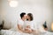 Happy pregnant couple relaxing on white bed and holding belly bump. Happy young husband kissing his smiling wife and hugging baby