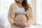 Happy Pregnant Woman sitting on bed holding and stroking apply cream on big belly for beauty moisturizing skin at home,Pregnancy