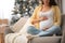 Happy pregnant woman on sofa in room decorated for Christmas, closeup. Expecting baby