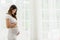 Happy Pregnant Woman standing in front of windows and stroking her big belly with love at cozy home,Pregnancy of young woman enjoy