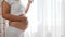 Happy pregnant woman in T-shirt touches naked belly and keeps glass with fresh water on white background