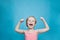 Happy pretten girl do sports and show muscles biceps on blue background.