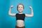 Happy pretten girl do sports and show muscles biceps on blue background.