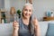 Happy pretty caucasian senior gray-haired female holds glass of water and shows thumb up