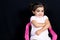 Happy pretty child girl sit on pink seat on black background with copy space