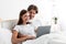 Happy pretty millennial caucasian lady and guy look at laptop chatting or making video call on bed