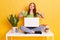 Happy pretty woman working with computer while sitting on white desk with crossed legs, lady wearing casual attire, showing thumbs