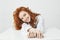 Happy pretty young girl with foxy hair smiling looking at camera sitting at table over white background.