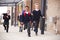 Happy primary school kids, wearing school uniforms and backpacks, running on a walkway outside their school building, front view,